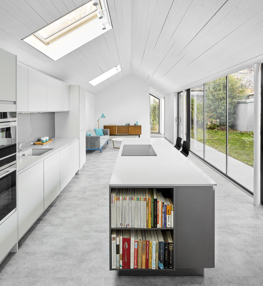 Photo of a contemporary open plan kitchen in Edinburgh with a single-bowl sink, flat-panel cabinets, white cabinets, grey splashback, with island, grey floor and white benchtop.