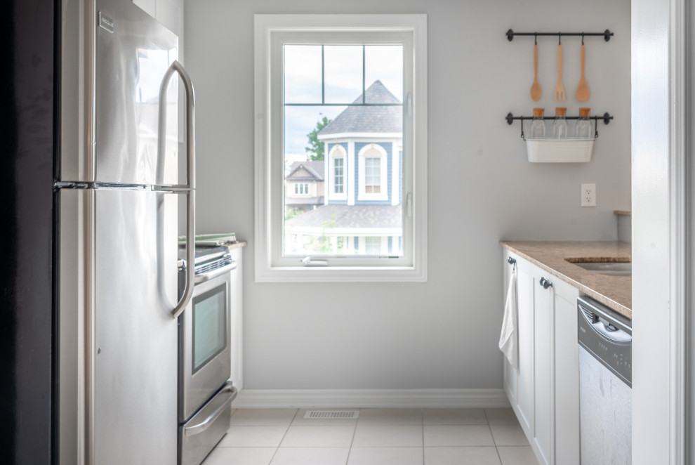 Small contemporary galley kitchen in Ottawa with a drop-in sink, shaker cabinets, white cabinets, granite benchtops, grey splashback, subway tile splashback, stainless steel appliances, laminate floors, brown floor and beige benchtop.