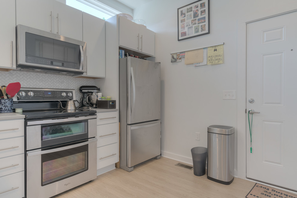 Small minimalist l-shaped vinyl floor and beige floor open concept kitchen photo with an undermount sink, flat-panel cabinets, white cabinets, quartz countertops, gray backsplash, marble backsplash, stainless steel appliances and a peninsula