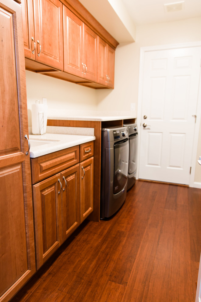 Large traditional single-wall utility room in Seattle with an undermount sink, raised-panel cabinets, medium wood cabinets, solid surface benchtops, beige walls, bamboo floors, a side-by-side washer and dryer and brown floor.