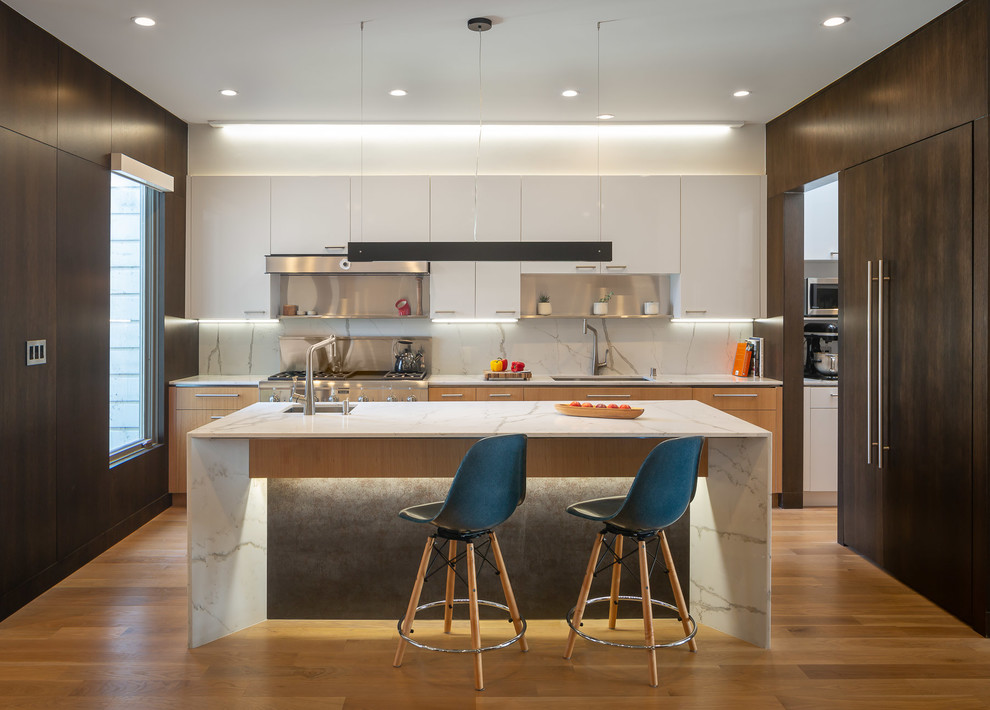 This is an example of a large midcentury kitchen in San Francisco with an undermount sink, flat-panel cabinets, white cabinets, marble benchtops, white splashback, stone slab splashback, with island, white benchtop, stainless steel appliances and light hardwood floors.