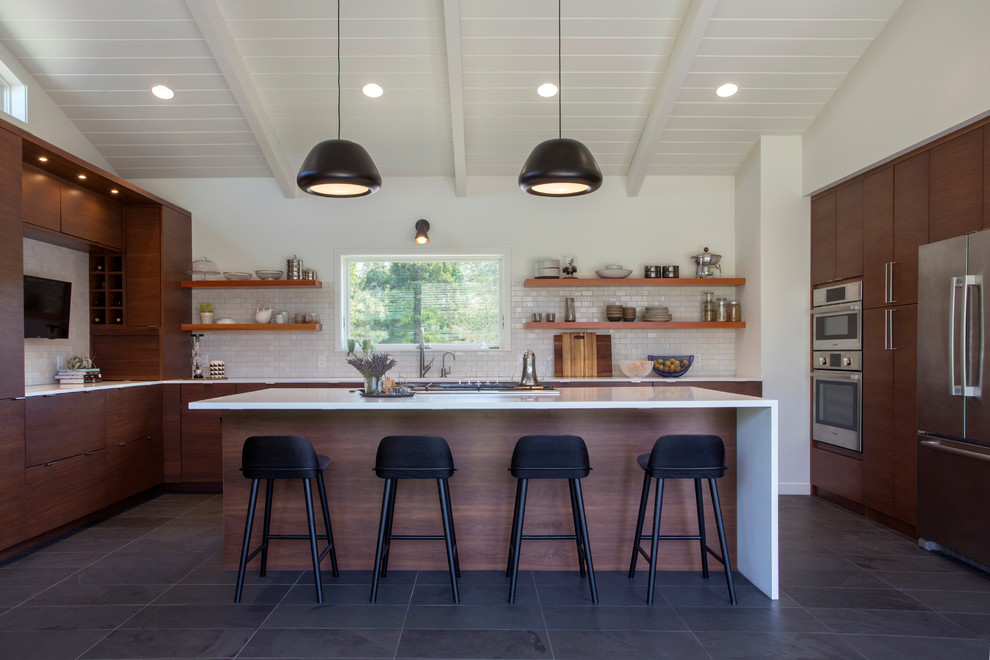 Midcentury open plan kitchen in San Francisco with flat-panel cabinets, dark wood cabinets, white splashback, subway tile splashback, stainless steel appliances, with island, grey floor and slate floors.