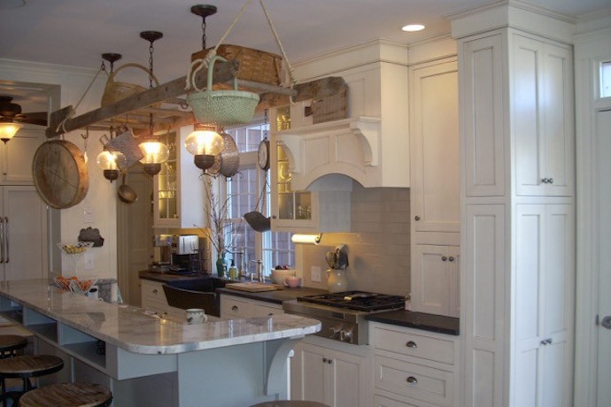 Large transitional l-shaped travertine floor and beige floor eat-in kitchen photo in Boston with recessed-panel cabinets, white cabinets, granite countertops, white backsplash, an island, black countertops, a farmhouse sink, subway tile backsplash and paneled appliances