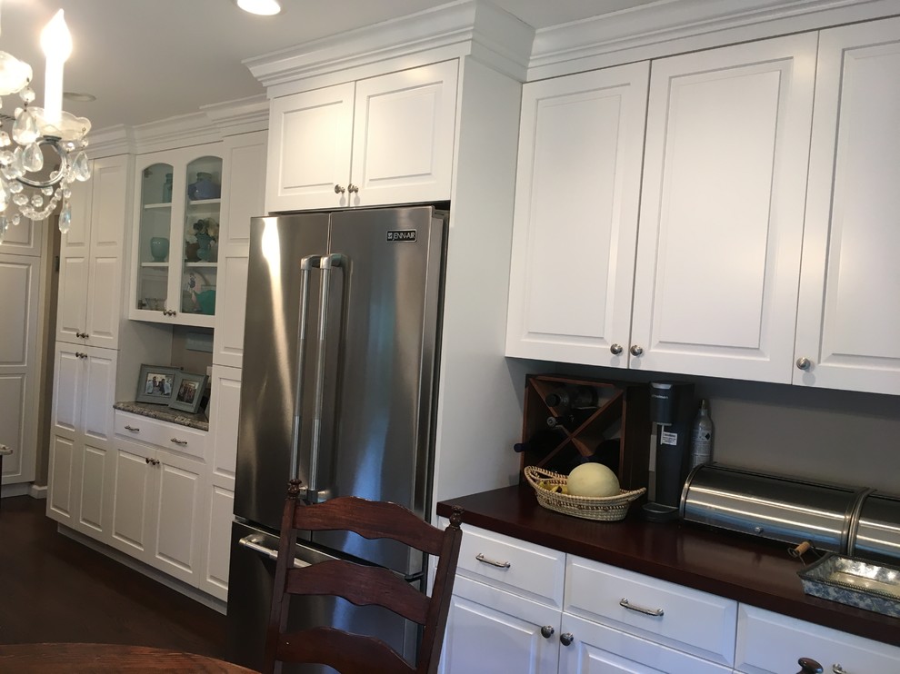 This is an example of a mid-sized transitional u-shaped eat-in kitchen in New York with raised-panel cabinets, white cabinets, stainless steel appliances, with island, an undermount sink, granite benchtops, beige splashback, ceramic splashback, dark hardwood floors and brown floor.