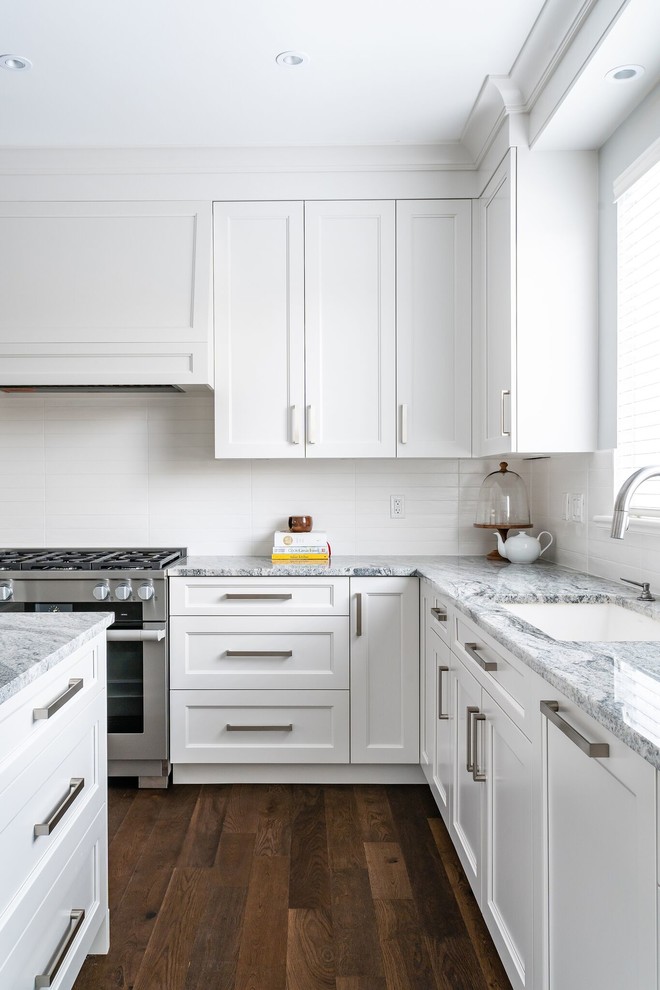Large transitional u-shaped eat-in kitchen in Vancouver with an undermount sink, white cabinets, granite benchtops, white splashback, subway tile splashback, stainless steel appliances, medium hardwood floors, with island, brown floor, multi-coloured benchtop and shaker cabinets.
