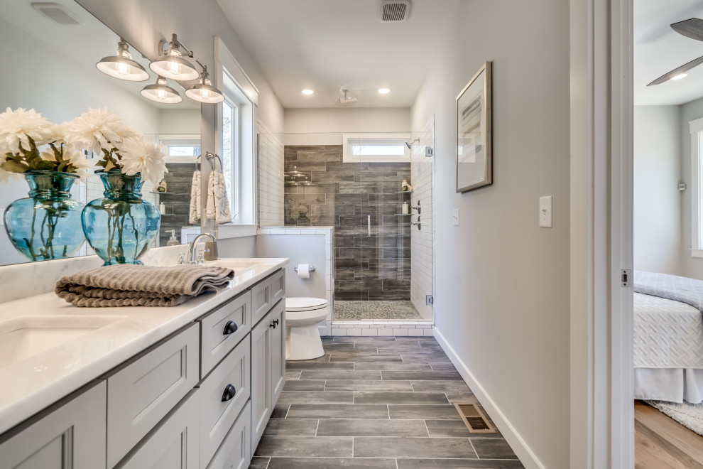 This is an example of a mid-sized transitional master bathroom in Raleigh with shaker cabinets, grey cabinets, an alcove shower, a two-piece toilet, black and white tile, subway tile, grey walls, porcelain floors, an undermount sink, solid surface benchtops, a hinged shower door, white benchtops and grey floor.