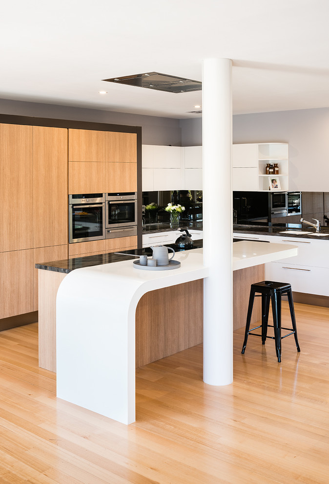 Inspiration for a large contemporary l-shaped open plan kitchen in Melbourne with a double-bowl sink, flat-panel cabinets, light wood cabinets, solid surface benchtops, mirror splashback, stainless steel appliances, light hardwood floors and with island.