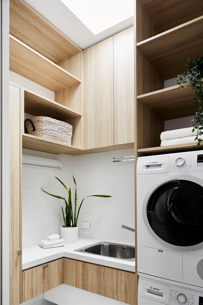 This is an example of a small contemporary l-shaped dedicated laundry room in Melbourne with a drop-in sink, beaded inset cabinets, light wood cabinets, marble benchtops, white walls, ceramic floors, a stacked washer and dryer, white floor and white benchtop.