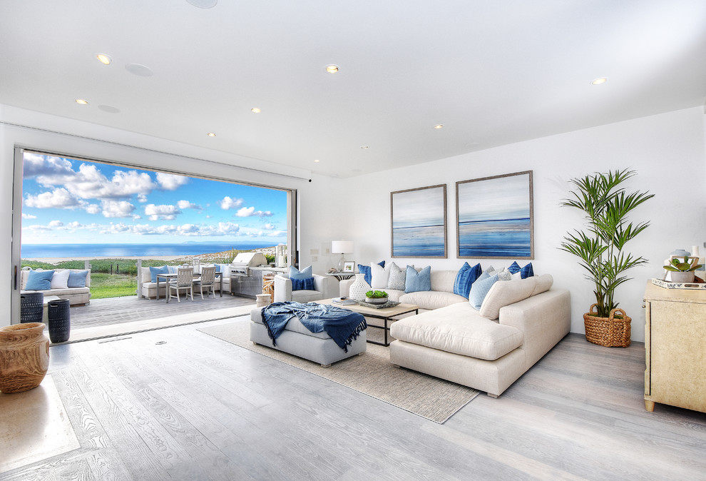 Large beach style open concept light wood floor and gray floor living room photo in Orange County with white walls, a standard fireplace, a wall-mounted tv and a stone fireplace