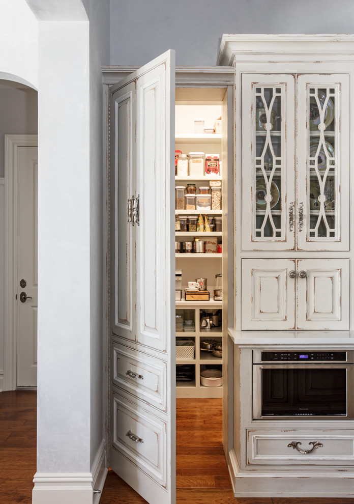 This is an example of a large traditional u-shaped kitchen pantry in Jacksonville with a farmhouse sink, beaded inset cabinets, white cabinets, quartz benchtops, white splashback, stone slab splashback, stainless steel appliances, medium hardwood floors, with island and brown floor.