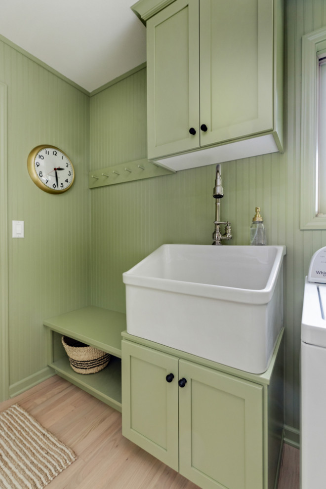 Inspiration for an expansive country galley dedicated laundry room in Other with a farmhouse sink, shaker cabinets, green cabinets, quartzite benchtops, green walls, light hardwood floors, a side-by-side washer and dryer and white benchtop.