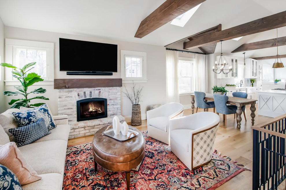 Design ideas for a mid-sized transitional open concept living room in Denver with grey walls, light hardwood floors, a standard fireplace, a brick fireplace surround, a wall-mounted tv, brown floor and vaulted.