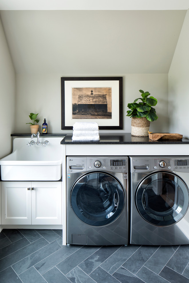 Inspiration for a transitional gray floor dedicated laundry room remodel in Minneapolis with recessed-panel cabinets, white cabinets, a side-by-side washer/dryer, a farmhouse sink, black countertops and gray walls