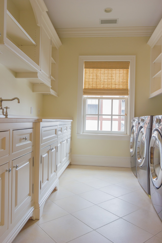 Photo of a large traditional galley dedicated laundry room in New York with white cabinets, a side-by-side washer and dryer and beige walls.