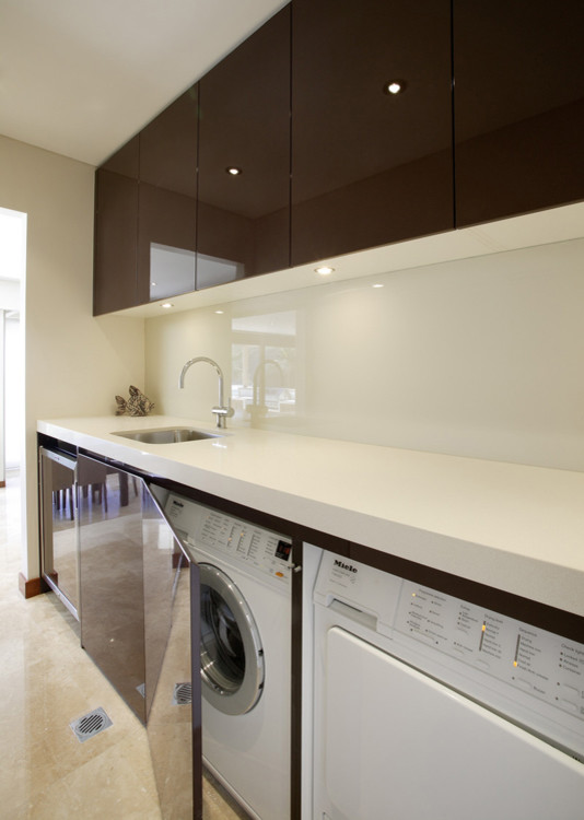 Small contemporary single-wall dedicated laundry room in Sydney with an undermount sink, flat-panel cabinets, brown cabinets, quartzite benchtops, white walls, limestone floors and a concealed washer and dryer.