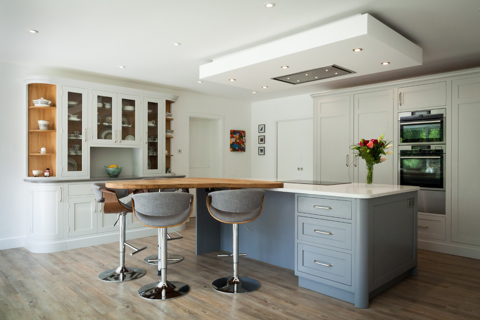 Mid-sized transitional u-shaped eat-in kitchen in Surrey with shaker cabinets, grey cabinets, quartz benchtops, stainless steel appliances, vinyl floors, with island, brown floor, white splashback and white benchtop.