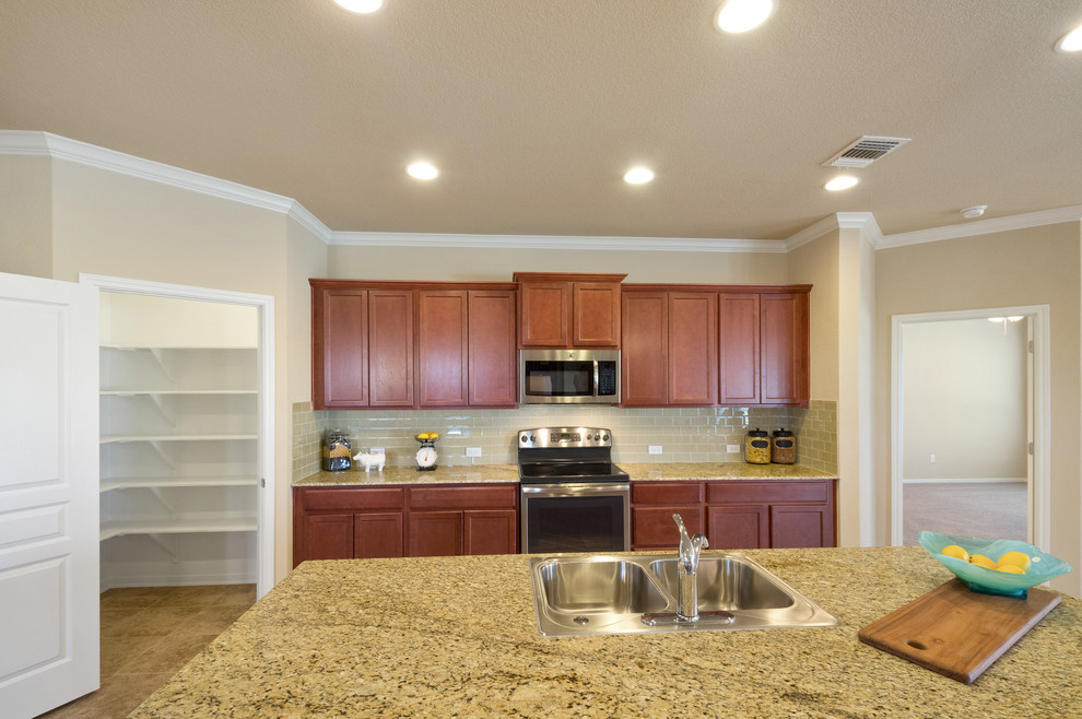 Large transitional l-shaped open plan kitchen in Austin with a drop-in sink, recessed-panel cabinets, medium wood cabinets, granite benchtops, beige splashback, glass tile splashback, stainless steel appliances, ceramic floors, with island and brown floor.