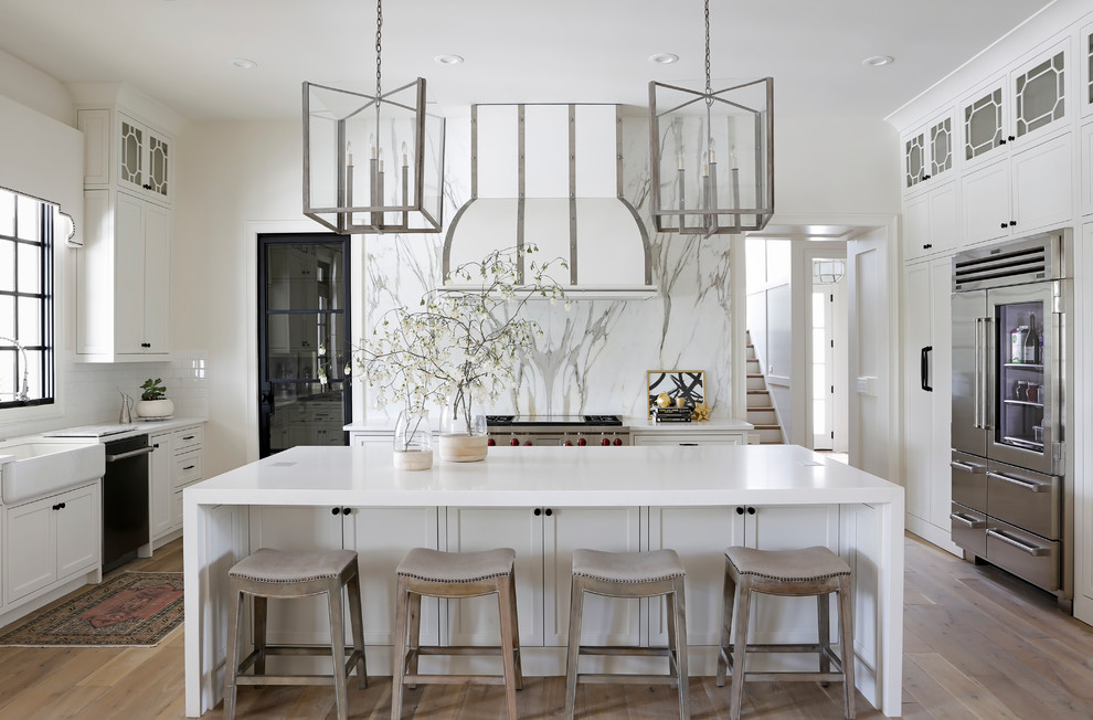 Inspiration for a transitional kitchen in Nashville with a farmhouse sink, shaker cabinets, white splashback, stainless steel appliances, light hardwood floors and with island.