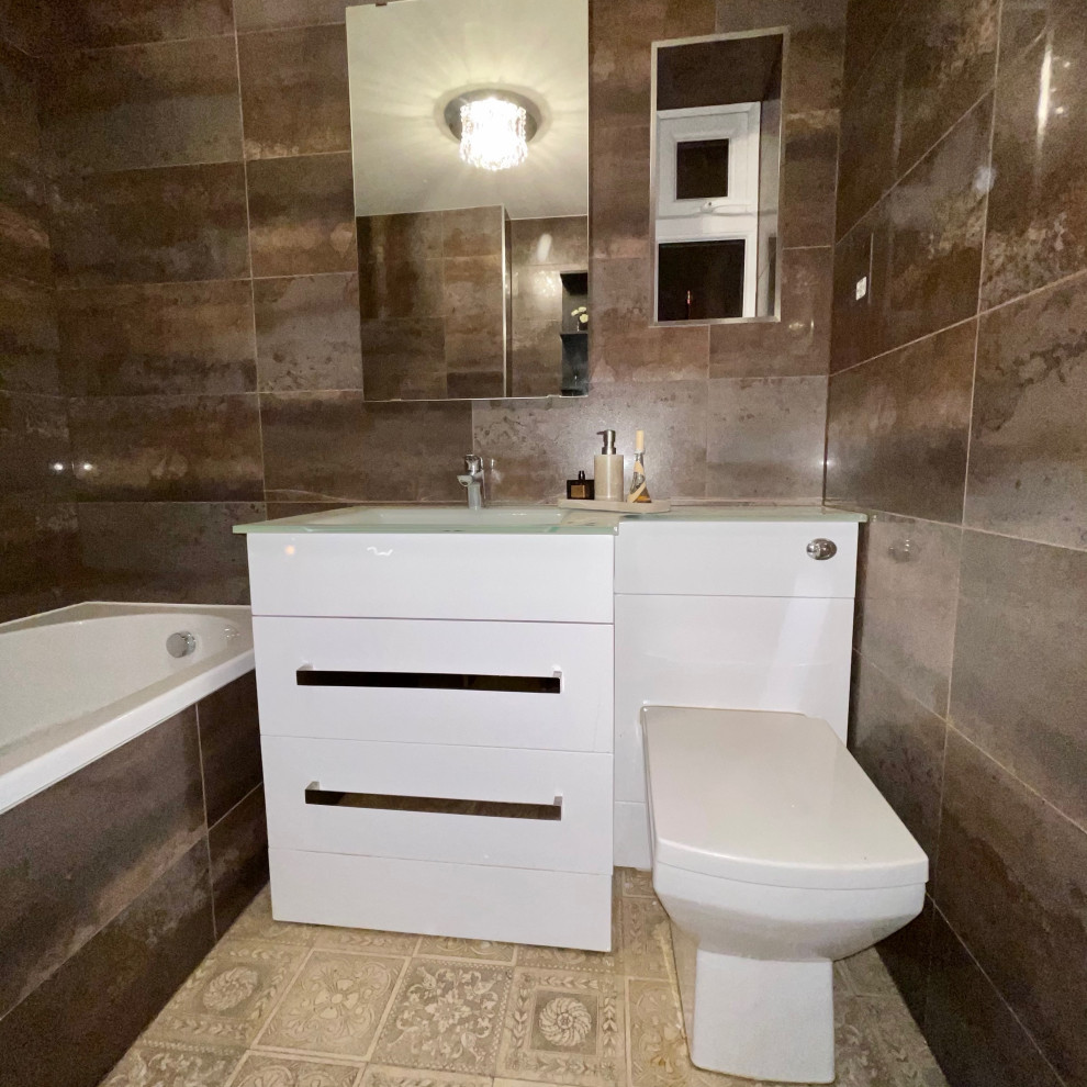 This is an example of a mid-sized modern bathroom in Buckinghamshire with flat-panel cabinets, white cabinets, a drop-in tub, a wall-mount toilet, porcelain tile, porcelain floors, an integrated sink, glass benchtops, brown floor, white benchtops, a niche, a single vanity and a freestanding vanity.