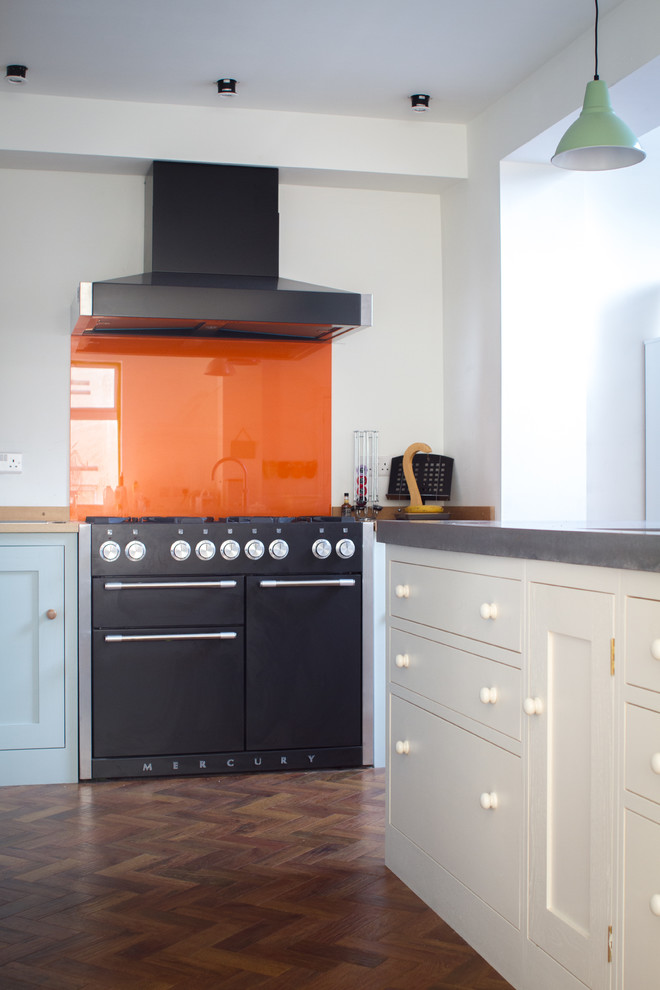 This is an example of a mid-sized arts and crafts l-shaped eat-in kitchen in Other with shaker cabinets, green cabinets, concrete benchtops, black appliances, dark hardwood floors, with island, orange splashback and glass sheet splashback.