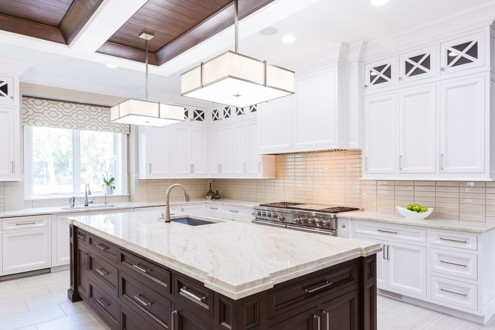 Expansive transitional l-shaped open plan kitchen in Chicago with an undermount sink, recessed-panel cabinets, white cabinets, marble benchtops, beige splashback, subway tile splashback, stainless steel appliances, porcelain floors, multiple islands, beige floor and beige benchtop.