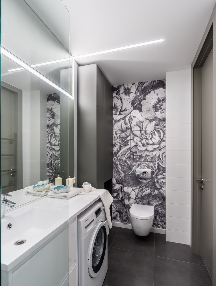 This is an example of a contemporary 3/4 bathroom in Saint Petersburg with a wall-mount toilet, an integrated sink, grey floor, flat-panel cabinets, white cabinets, white tile and a laundry.