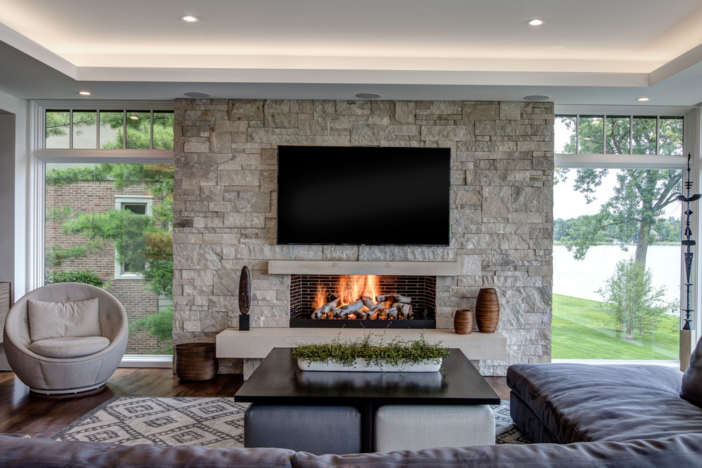 Inspiration for a mid-sized transitional enclosed family room in Detroit with white walls, dark hardwood floors, a standard fireplace, a stone fireplace surround, a wall-mounted tv and brown floor.
