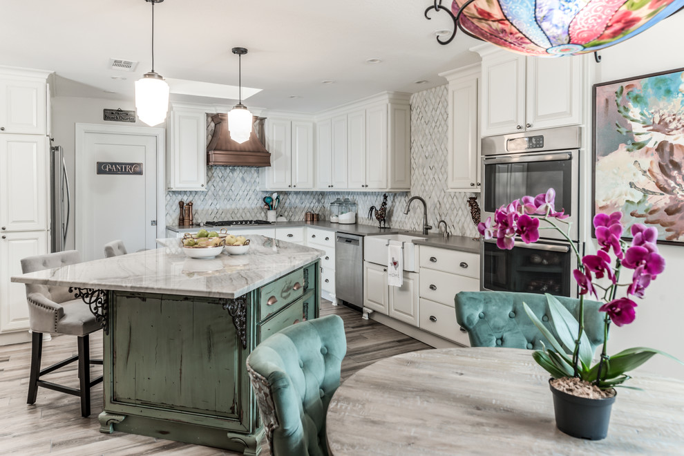 This is an example of a large traditional l-shaped eat-in kitchen in Houston with a farmhouse sink, raised-panel cabinets, white cabinets, quartz benchtops, white splashback, marble splashback, stainless steel appliances, porcelain floors, with island, brown floor and grey benchtop.