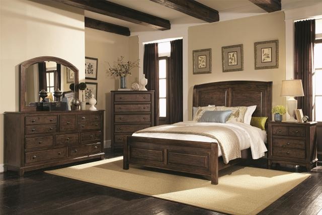 Modelo de dormitorio principal rústico de tamaño medio con paredes beige, suelo de madera oscura, todas las chimeneas y marco de chimenea de hormigón