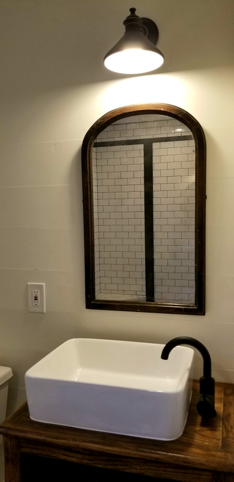 Photo of a mid-sized eclectic powder room in Little Rock with furniture-like cabinets, medium wood cabinets, a one-piece toilet, white tile, subway tile, white walls, a vessel sink and wood benchtops.