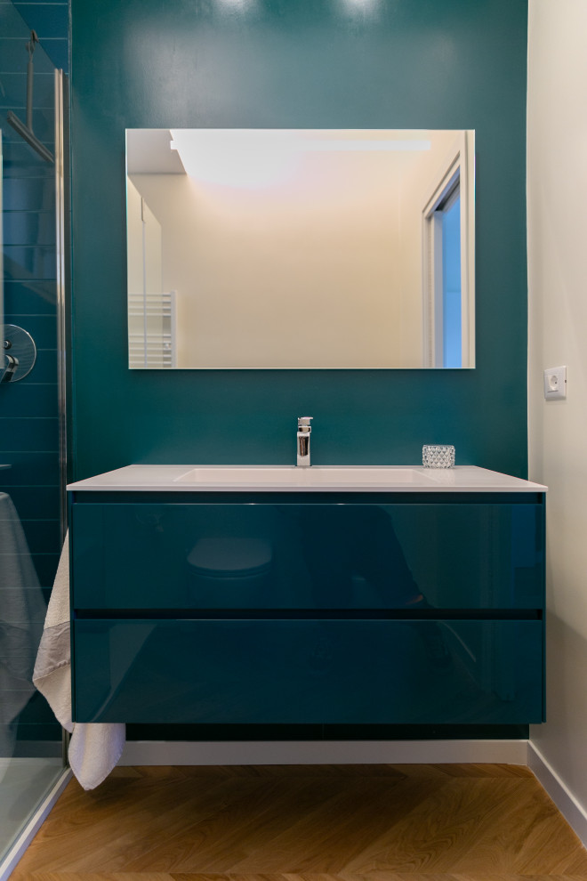 This is an example of a mid-sized modern 3/4 bathroom in Rome with flat-panel cabinets, blue cabinets, a curbless shower, a two-piece toilet, blue tile, matchstick tile, blue walls, light hardwood floors, an integrated sink, quartzite benchtops, white benchtops, a single vanity and a freestanding vanity.