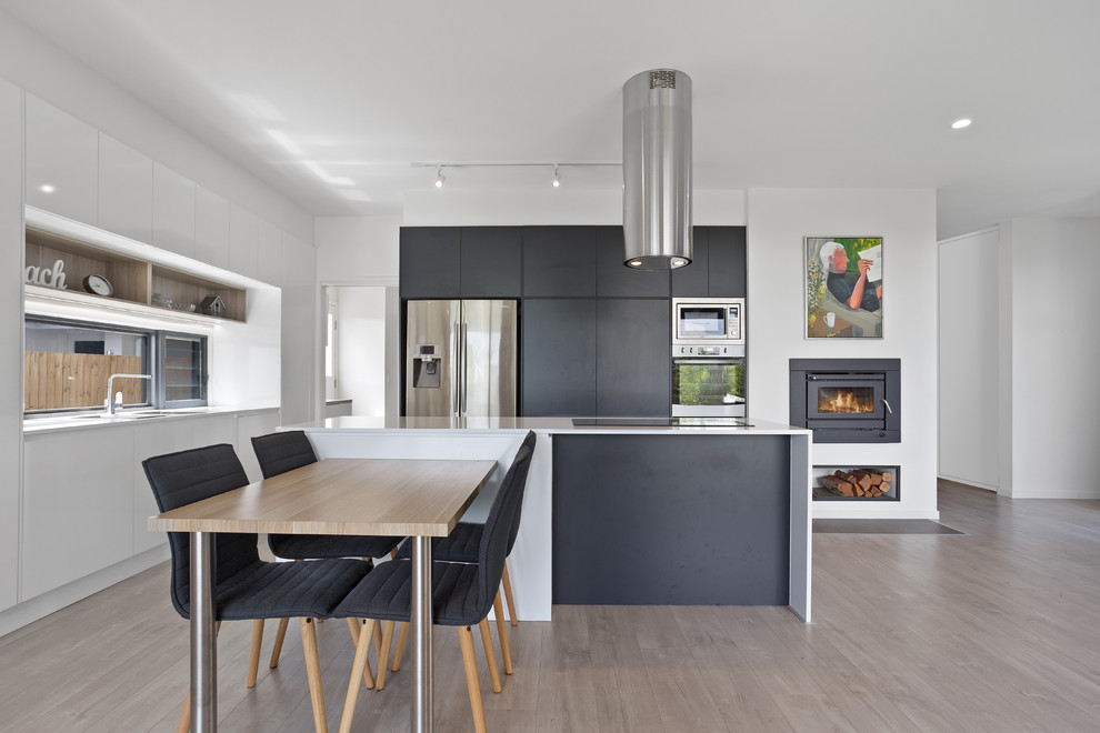 This is an example of a contemporary l-shaped eat-in kitchen in Sunshine Coast with a double-bowl sink, flat-panel cabinets, black cabinets, stainless steel appliances, light hardwood floors, with island, beige floor and white benchtop.