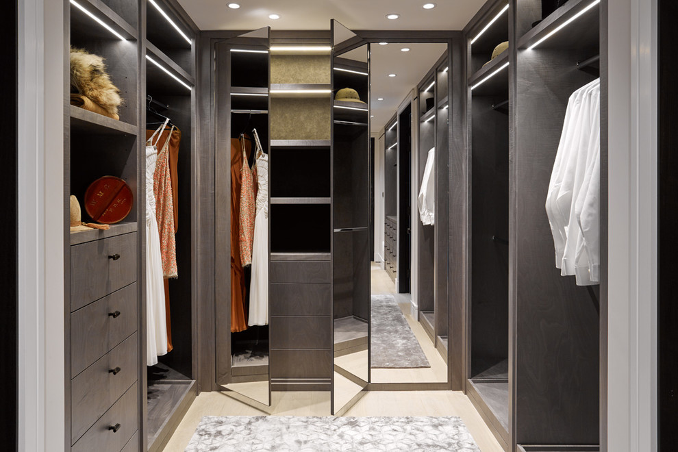 This is an example of a contemporary gender-neutral walk-in wardrobe in London with open cabinets, medium wood cabinets, light hardwood floors and beige floor.