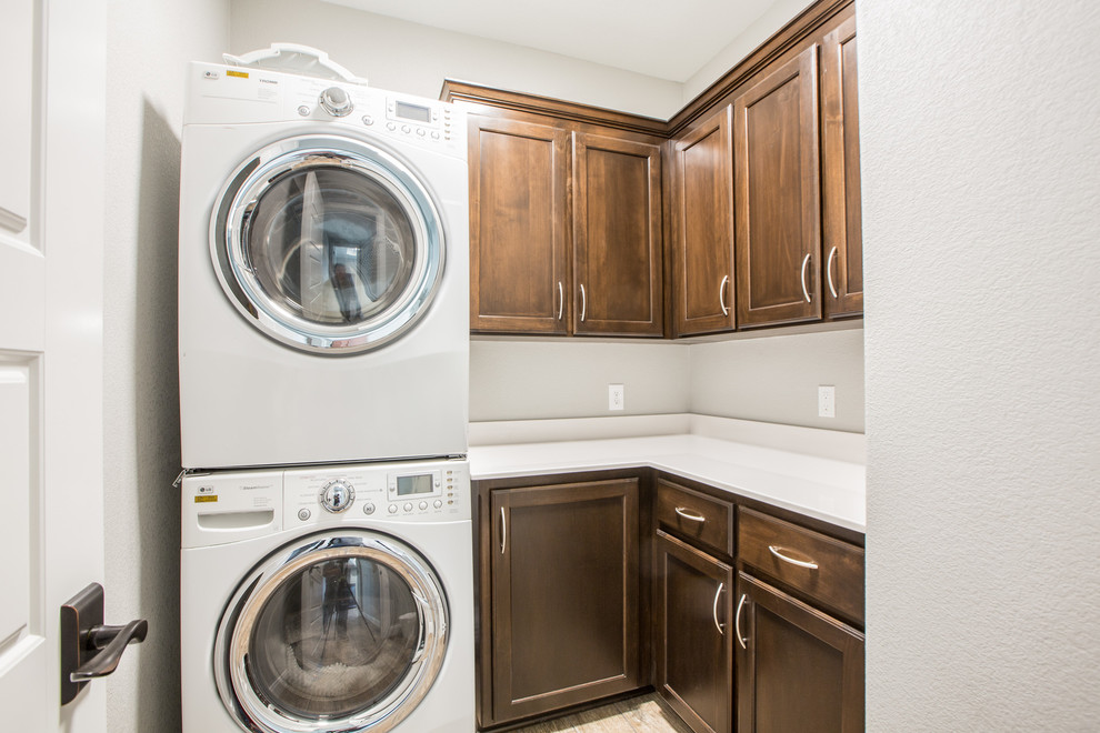 Design ideas for a mid-sized transitional l-shaped dedicated laundry room in Dallas with shaker cabinets, dark wood cabinets, quartz benchtops, grey walls, medium hardwood floors and a stacked washer and dryer.