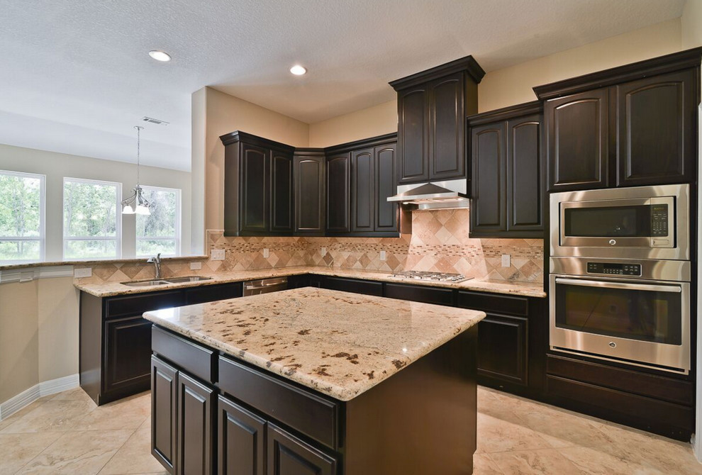 Mid-sized transitional u-shaped travertine floor enclosed kitchen photo in Houston with a double-bowl sink, raised-panel cabinets, dark wood cabinets, granite countertops, beige backsplash, ceramic backsplash, stainless steel appliances and an island