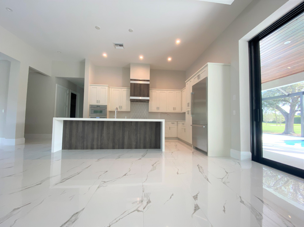 Inspiration for a mid-sized transitional l-shaped porcelain tile and white floor open concept kitchen remodel in Miami with an undermount sink, recessed-panel cabinets, beige cabinets, quartz countertops, white backsplash, porcelain backsplash, stainless steel appliances, an island and white countertops