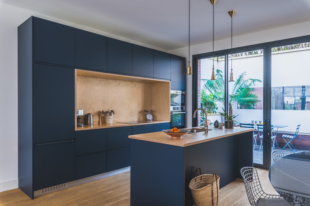 Inspiration for a contemporary galley eat-in kitchen in Paris with a double-bowl sink, flat-panel cabinets, blue cabinets, wood benchtops, brown splashback, timber splashback, panelled appliances, medium hardwood floors, with island, brown floor and brown benchtop.