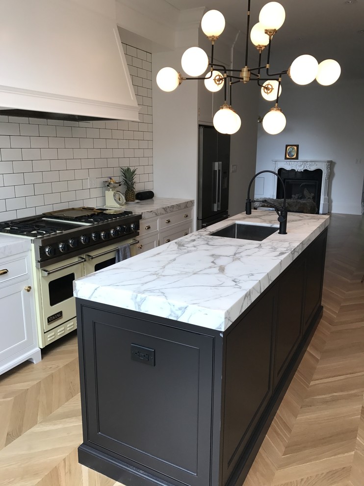 This is an example of a mid-sized traditional single-wall open plan kitchen in Toronto with an undermount sink, shaker cabinets, white cabinets, marble benchtops, white splashback, subway tile splashback, coloured appliances, light hardwood floors, with island, brown floor and grey benchtop.