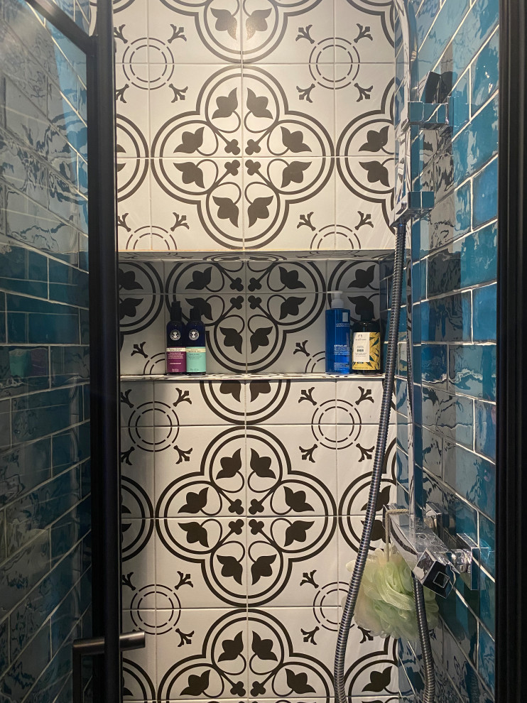 This is an example of a small eclectic master bathroom in London with white cabinets, an open shower, a one-piece toilet, blue tile, ceramic tile, black walls, ceramic floors, a drop-in sink, white floor, a hinged shower door, a niche, a single vanity, a built-in vanity and panelled walls.