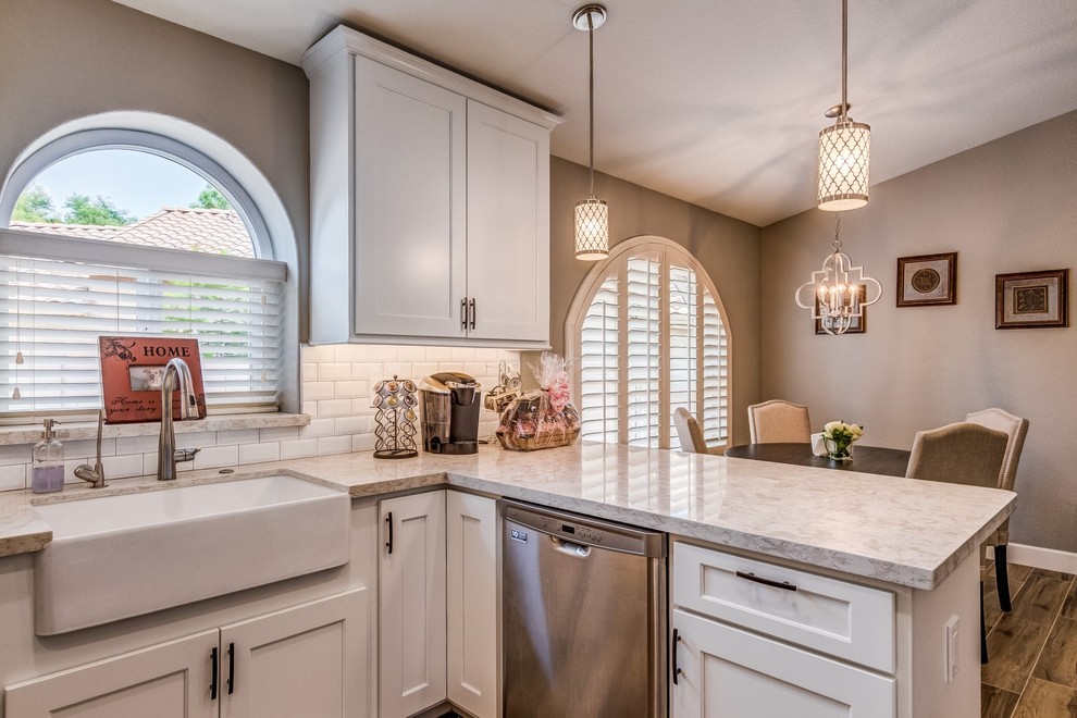 Example of a mid-sized transitional u-shaped porcelain tile and beige floor eat-in kitchen design in Phoenix with a farmhouse sink, shaker cabinets, white cabinets, quartz countertops, white backsplash, subway tile backsplash, stainless steel appliances and white countertops