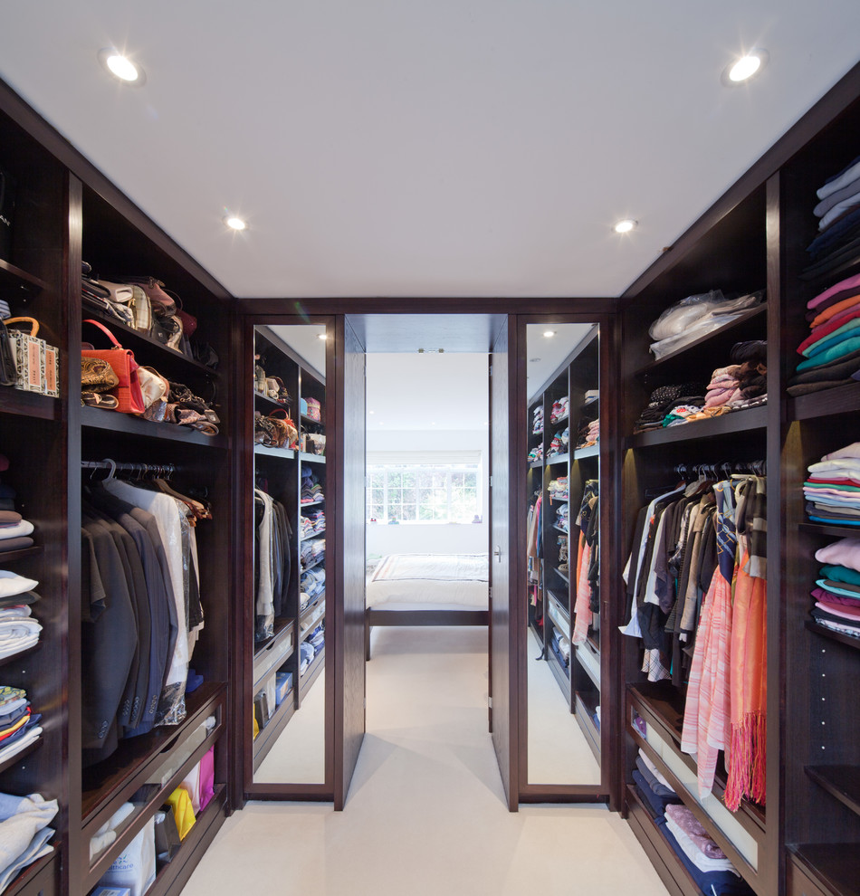 This is an example of a contemporary gender-neutral walk-in wardrobe in London with open cabinets and dark wood cabinets.