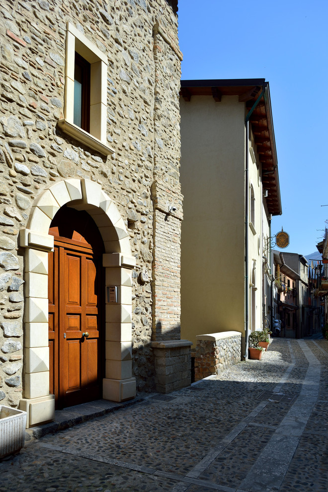 Photo of a mediterranean three-storey exterior in Other with stone veneer, a gable roof and a mixed roof.