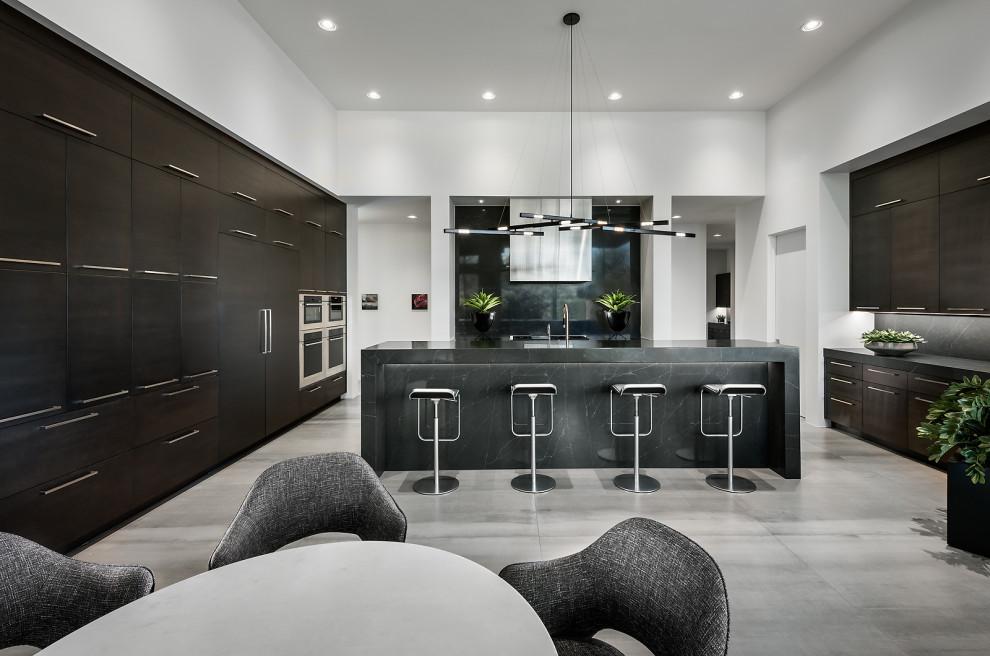Inspiration for an expansive contemporary kitchen in Phoenix with a submerged sink, flat-panel cabinets, dark wood cabinets, composite countertops, stainless steel appliances, an island, grey floors, black worktops and a feature wall.