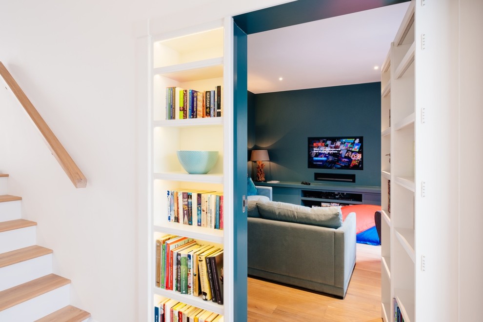 Mid-sized beach style enclosed home theatre in Gloucestershire with blue walls, light hardwood floors and a built-in media wall.