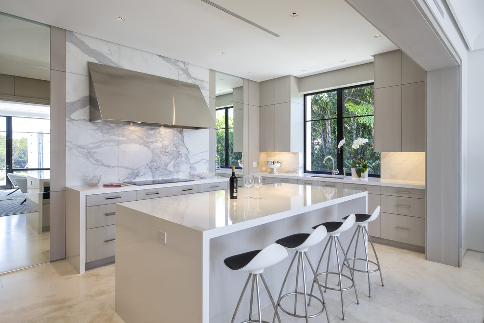 This is an example of a mid-sized contemporary open plan kitchen in Miami with an undermount sink, flat-panel cabinets, light wood cabinets, laminate benchtops, white splashback, stone slab splashback, marble floors, with island and stainless steel appliances.