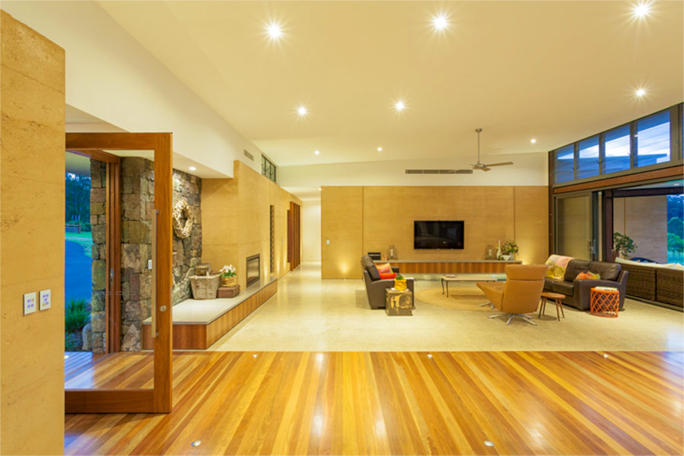 Inspiration for an expansive contemporary open concept living room in Brisbane with beige walls, concrete floors, a standard fireplace, a stone fireplace surround and a wall-mounted tv.