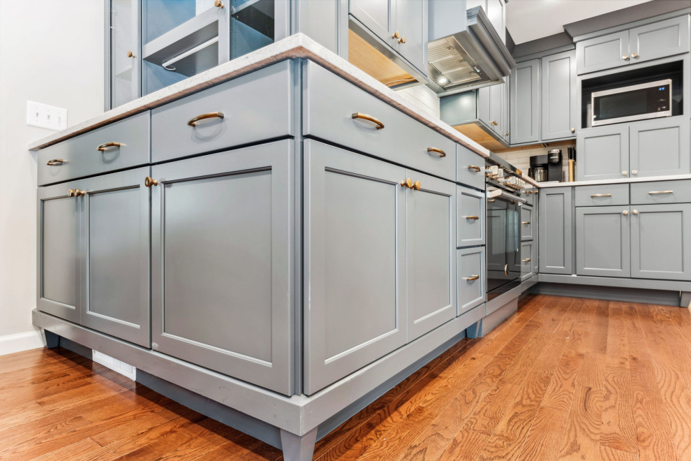 Inspiration for a small traditional l-shaped eat-in kitchen in Columbus with a farmhouse sink, shaker cabinets, blue cabinets, quartz benchtops, white splashback, porcelain splashback, stainless steel appliances, medium hardwood floors, no island, brown floor and white benchtop.