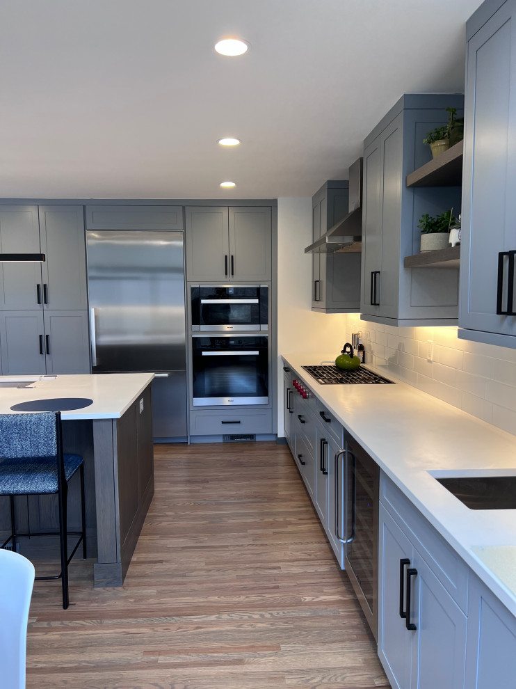 Große Moderne Küche in L-Form mit Schrankfronten im Shaker-Stil, grauen Schränken, Küchenrückwand in Weiß, Küchengeräten aus Edelstahl, Kücheninsel und weißer Arbeitsplatte in Sonstige