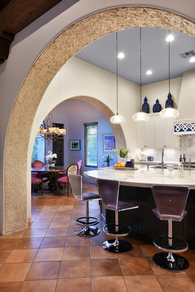 This is an example of a large mediterranean u-shaped eat-in kitchen in Phoenix with an undermount sink, recessed-panel cabinets, white cabinets, quartz benchtops, multi-coloured splashback, ceramic splashback, stainless steel appliances, terra-cotta floors, with island, orange floor and white benchtop.