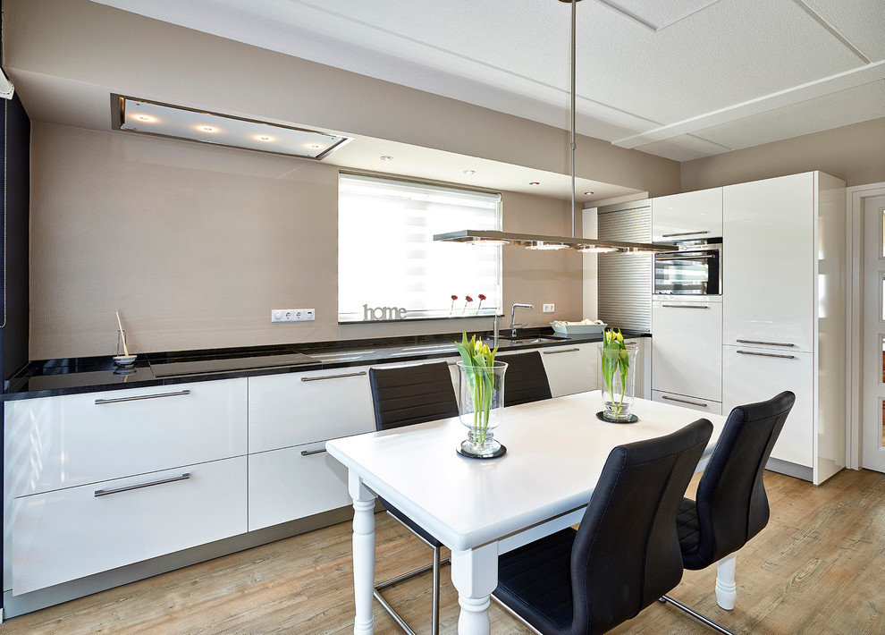 This is an example of a contemporary l-shaped eat-in kitchen in Other with an undermount sink, flat-panel cabinets, stainless steel appliances, light hardwood floors and beige splashback.
